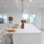 Modern island with pendant lighting, white solid stone counter, and white cabinets.
